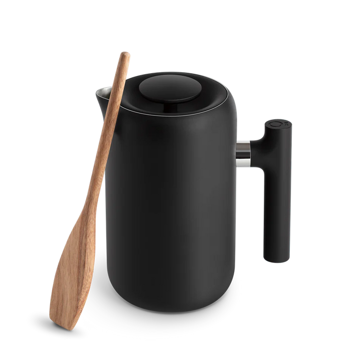 A black Fellow Clara French Press with a wooden stirrer beside it.